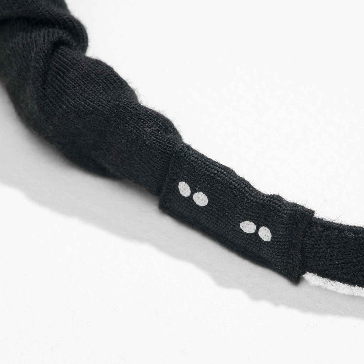 Close-up of a black headband fabric label with kooshoo branded white dots on a white background
#color_black
