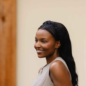 Woman with styled hair wearing a black ruffled fabric headband smiling against a neutral background
#color_black